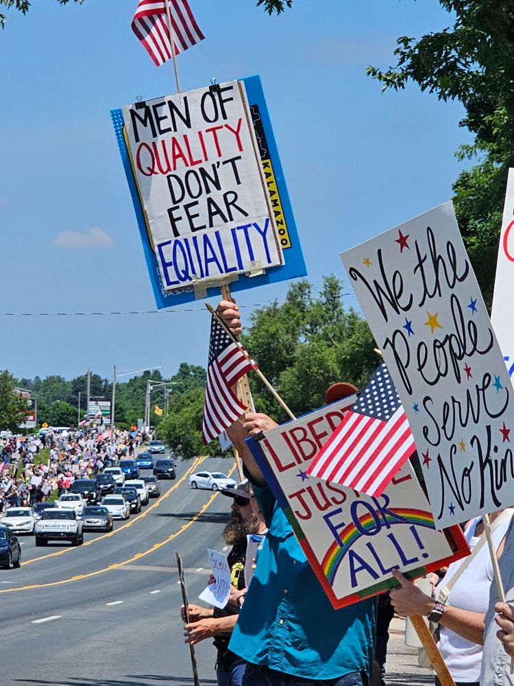 Protestors in Kalamazoo, MI holding signs that read, *Men of Quality Don't Fear Equality", "Liberty and Justice for All", and "We the people serve no king"