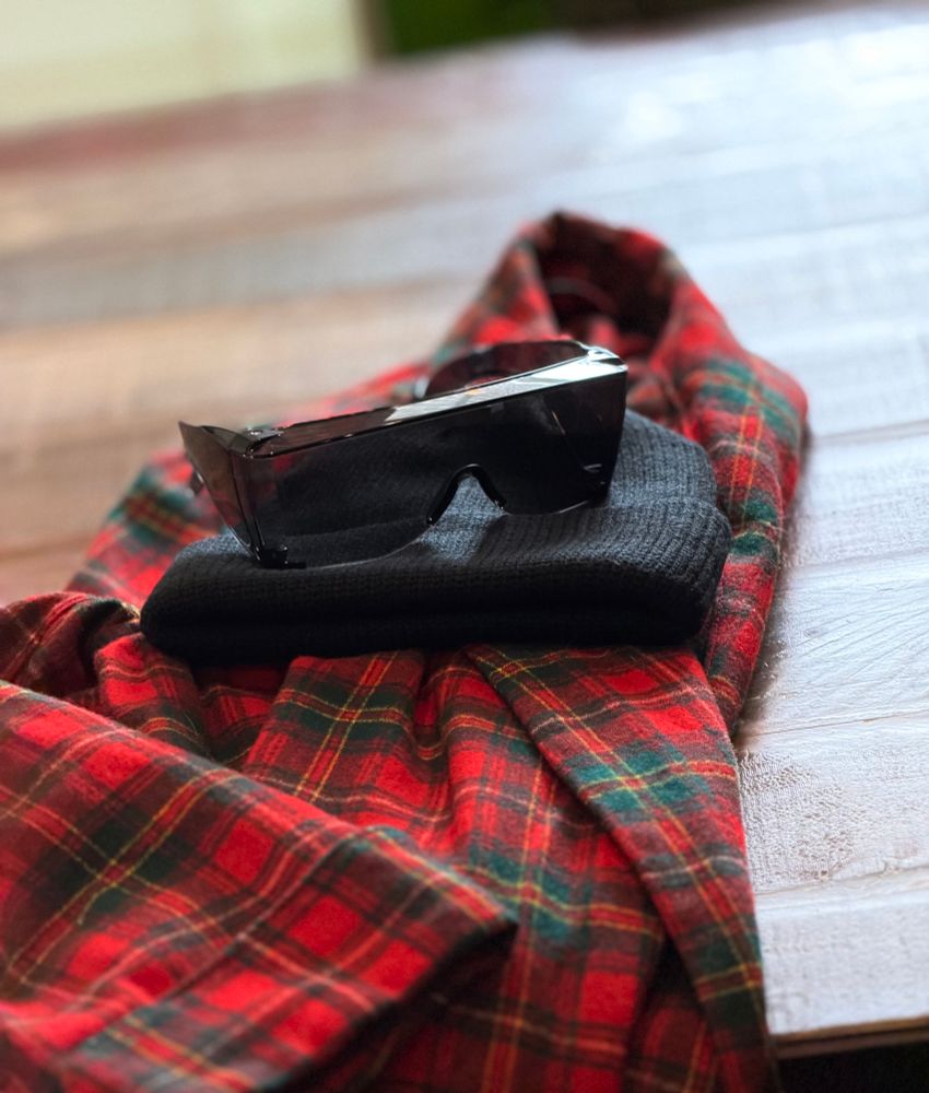 On an table: A plaid red vintage wool robe, a black beanie, and a pair of fit-over sunglasses.