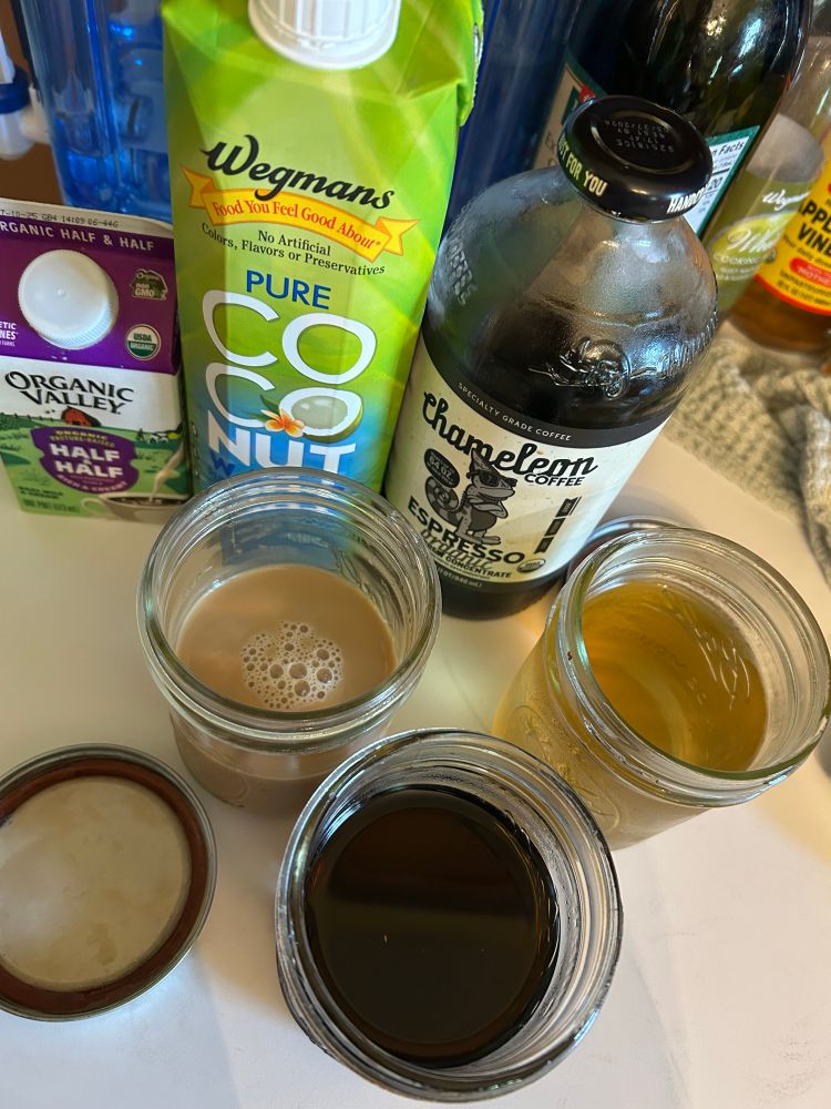Photo taken from above: lineup of half&half cream, coconut water, chameleon espresso cold brew concentrate, and three mason jars holding the coffee mixture and 2 syrups of mint and basil 