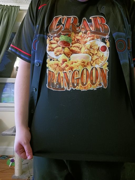 A close up of a person wearing a very gaudy t-shirt that says "Crab Rangoon" in big letters and a large photo of several plates of crab rangoons. It is something else.