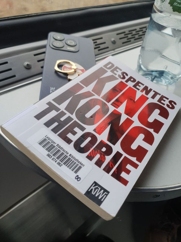 Foto of the book king Kong theory by virginie despentes, German translation. A phone, a water bottle. In a train
