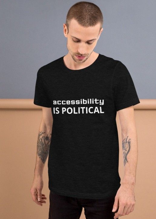 white tatooed dude wearing a black heather shirt with white text 'accessibility IS POLITICAL'