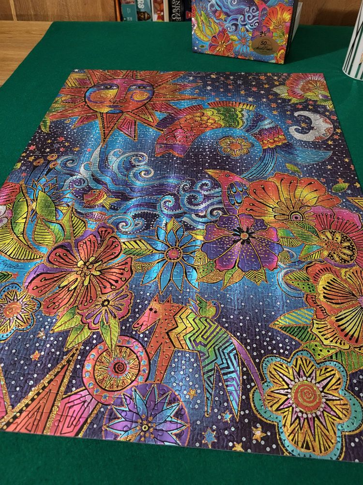 Buntes, psychedelisches 1000 Teile Puzzle mit leuchtenden Farben und goldenen Konturen. Es zeigt eine Sonne mit Gesicht, eine Mondsichel, bunte Blumen, abstrakte Tiere und Wellen auf dunkelblauem Hintergrund voller Sterne. Der Stil ist fantasievoll und kunstvoll verschnörkelt.