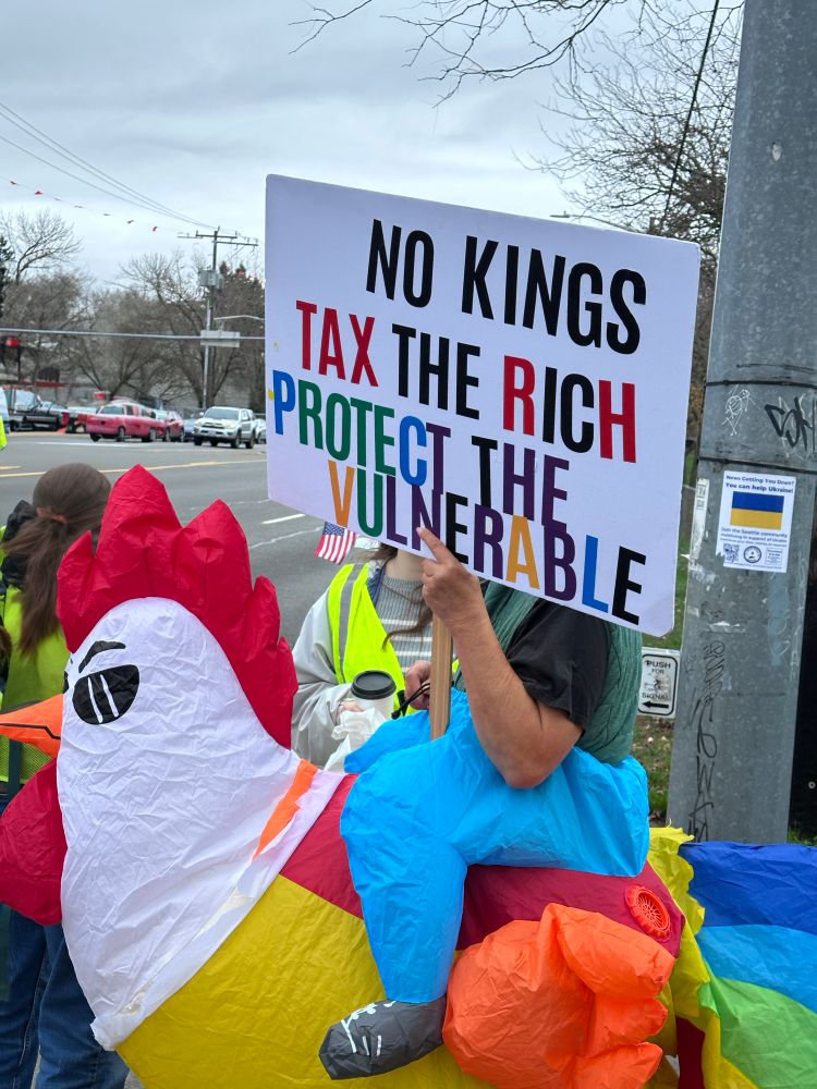Protestor with chicken inflatable at Seattle Tesla takedown with sign “no kings, tax the rich, protect the vulnerable”