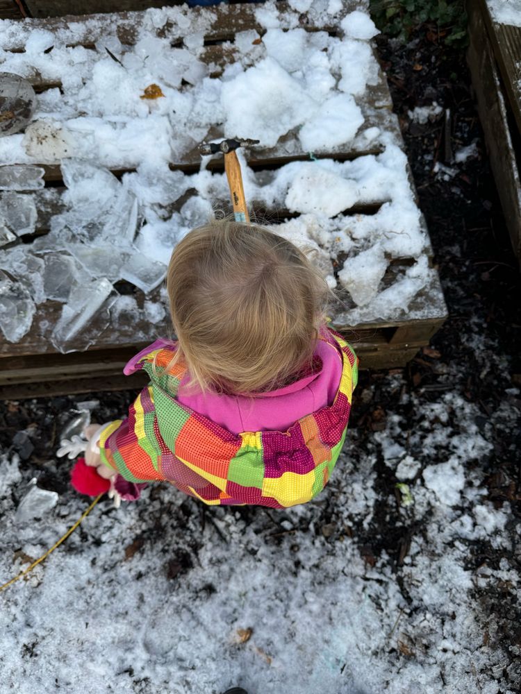 Toddler in a bright coat hammering ice 