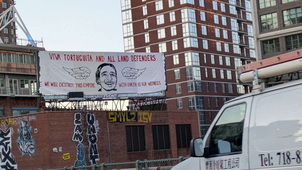 A banner over a billboard in Brooklyn reads viva Tortuguita and alland defenders/we will destroy the empire with earth as our witness