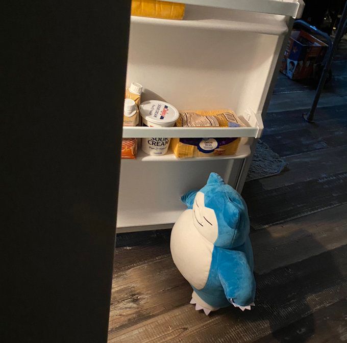 Picture of a Snorlax plush appearing to be getting into a refrigerator at night to get some food 