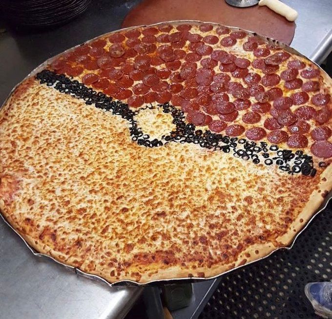 Picture of a massive pizza that is topped to look like a pokeball. Top half has pepperoni, the middle has olives going from left to right with it going in a small circle in the middle, bottom half is cheese. 