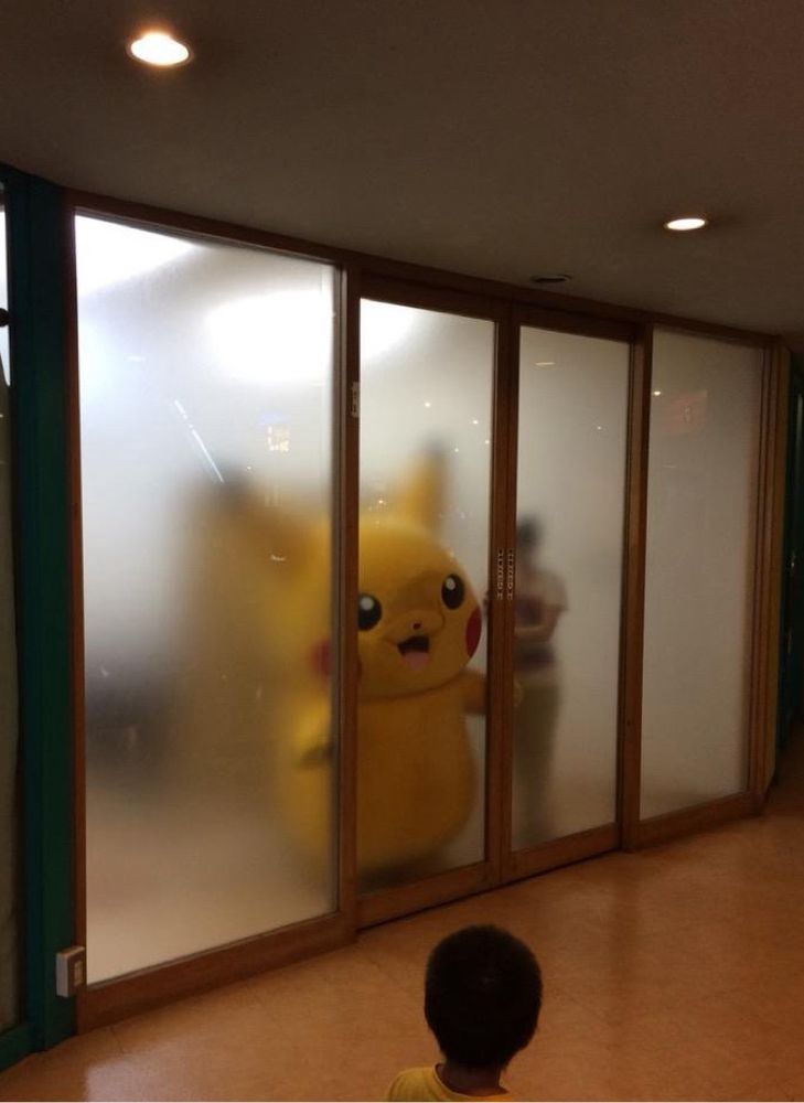 Picture of a person in pikachu mascot costume pressed up against a see through glass sliding door 