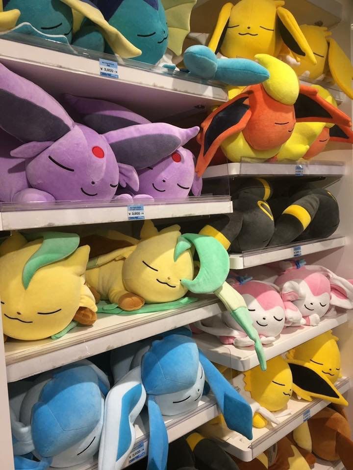 Photo of a bunch of sleepy eeveelution plushes on store shelves in a Pokémon center 