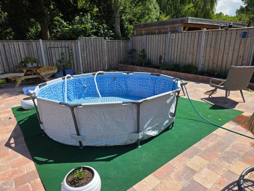 Een net opgezet zwembad met een tuinslang erin, op een kunstgrastapijt in onze achtertuin.