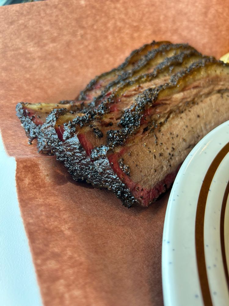 Close up of sliced brisket on a brown paper mat. You can see the  red ring around the border of the meat, just inside the black crust on the exterior. This stuff was like butter.