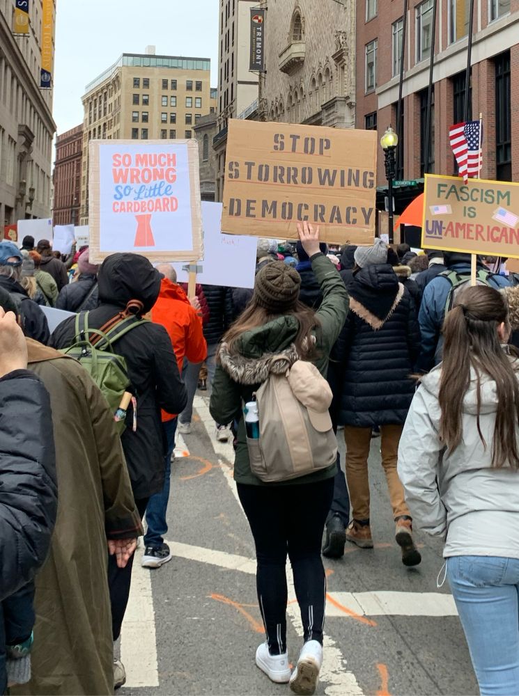 Photo of protester in Boston holding a sign that says “STOP STORROWING DEMOCRACY”