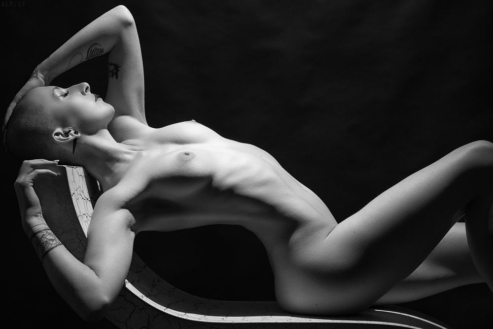 Nude female model with shaved head in a pool of light from above. 
