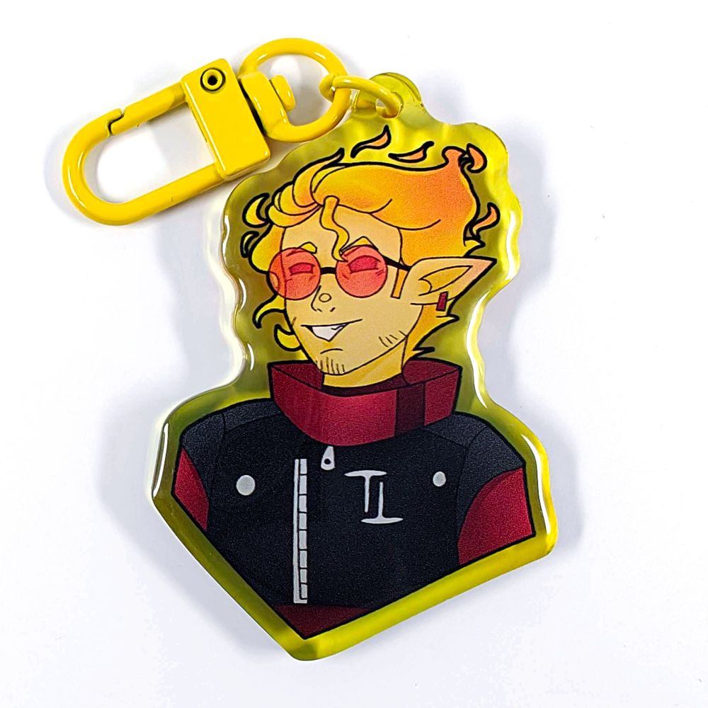 A picture of an acrylic keychain of TangoTek with his short fire hair. He is smirking, wearing round red sunglasses and a red and black outfit. The rim of the keychain is yellow and it has a bright yellow clasp.