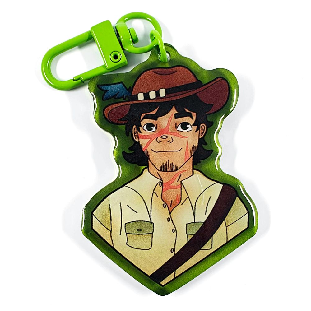 A picture of an acrylic keychain of GoodTimesWithScar with his jungle outfit. He is smiling, wearing a jungle brown hat and a beige shirt with two open buttons. The rim of the keychain is dark green and it has a bright green clasp.
