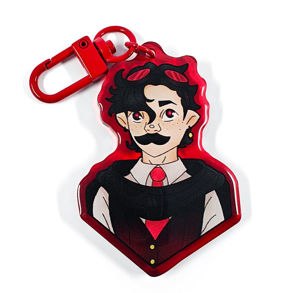 A picture of an acrylic keychain of MumboJumbo with his short, curly black hair. He has his usual thick mustache and is wearing a white shirt, a bright red tie and an over the shoulders black cape on top. The rim of the keychain is red and it has a bright red clasp.