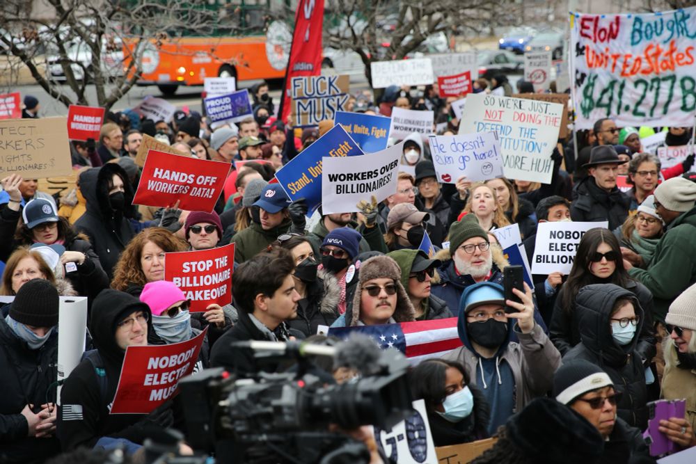 A photo of protestors in front of the Department of Labor, holding signs that says “AFGE” and “Hands of worker data.”