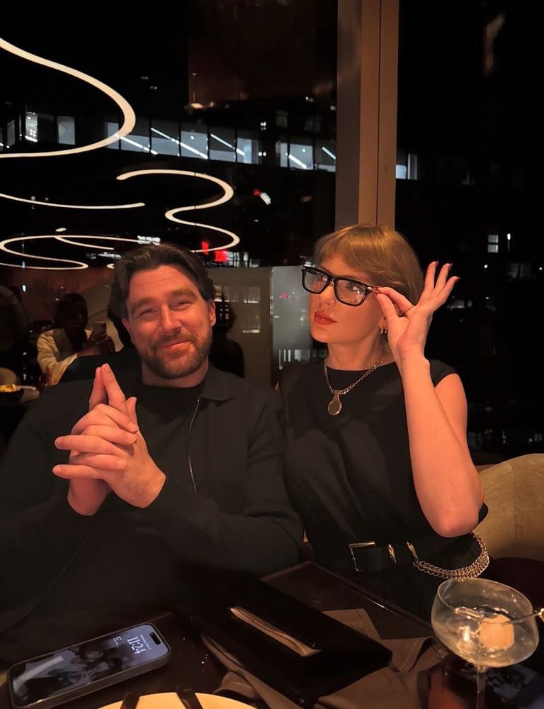 Taylor Swift and Travis Kelce on Travis’ most recent Instagram post. She is wearing glasses and holding them and he is making a pistol with his hands, they’re matching and having dinner. Travis’s phone is on the table, unlocked so we can see his lockscreen which is a picture of him and taylor