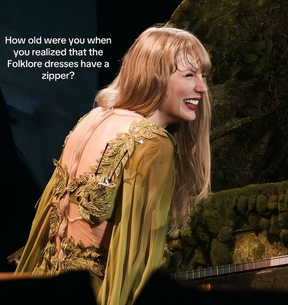 A picture of taylor swift’s back and she’s wearing the green folklore dress while sitting behind the evermore piano at the eras tour. It has a skin toned zipper running on the back of the dress