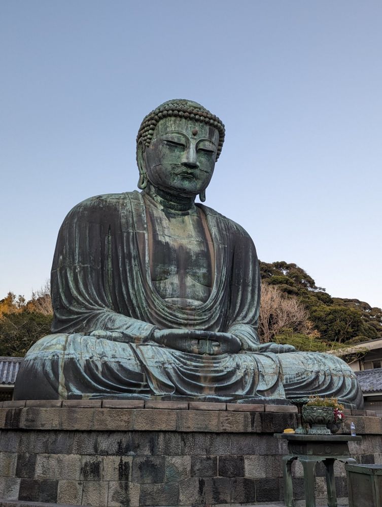 A large statue of Amida Buddha sits with legs crossed. Pale blue sky behind.