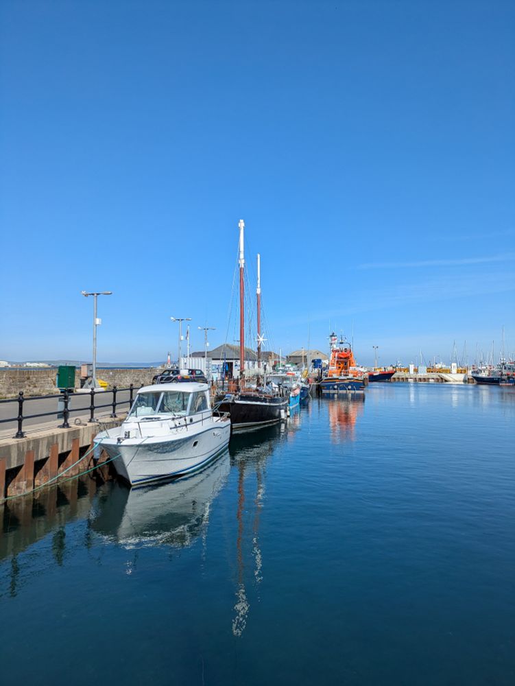 Harbour with blue sea and blue sky, boats moored on the left and in the distance.