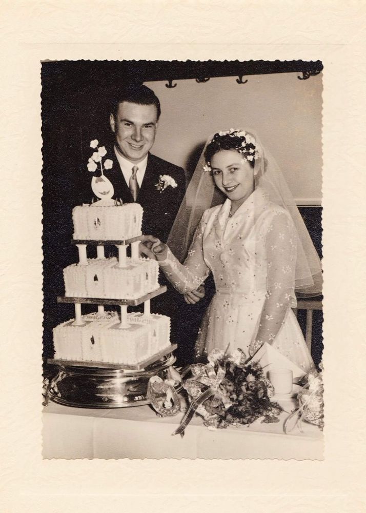 A wedding couple with their cake and a bouquet on the table.
