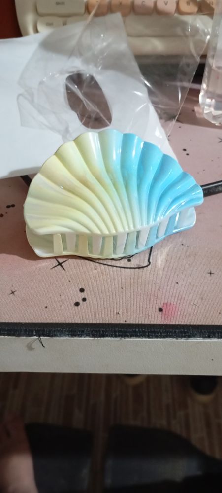 Uma presilha para cabelo em formato de concha. Ela é branca e azul. 