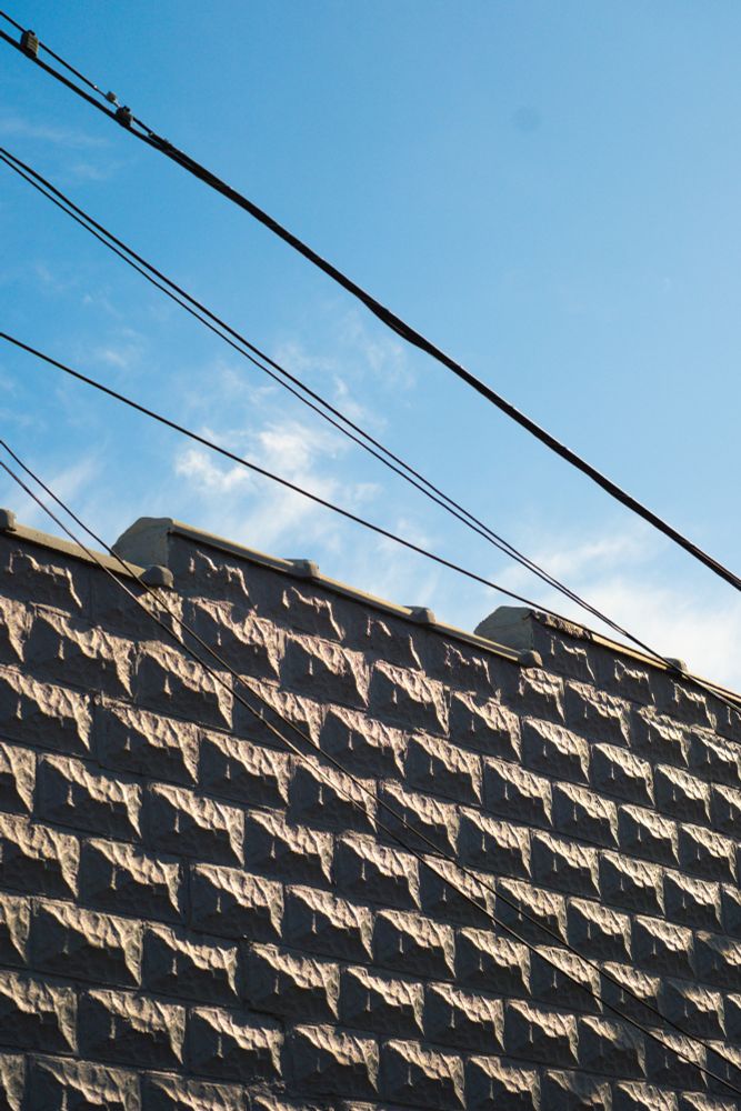A photo looking upward, where a gray brick wall can be seen with telephone wires interconnected
