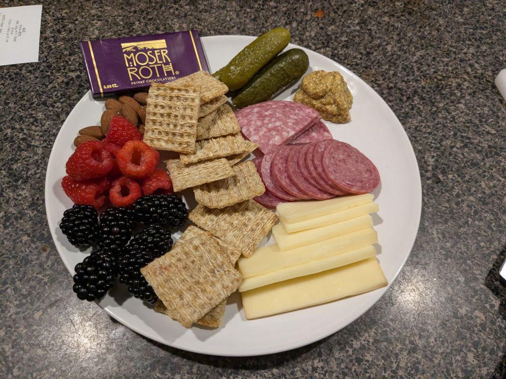 Snack plate with berries, cheese, salami, crackers, pickles, mustard and chocolate 