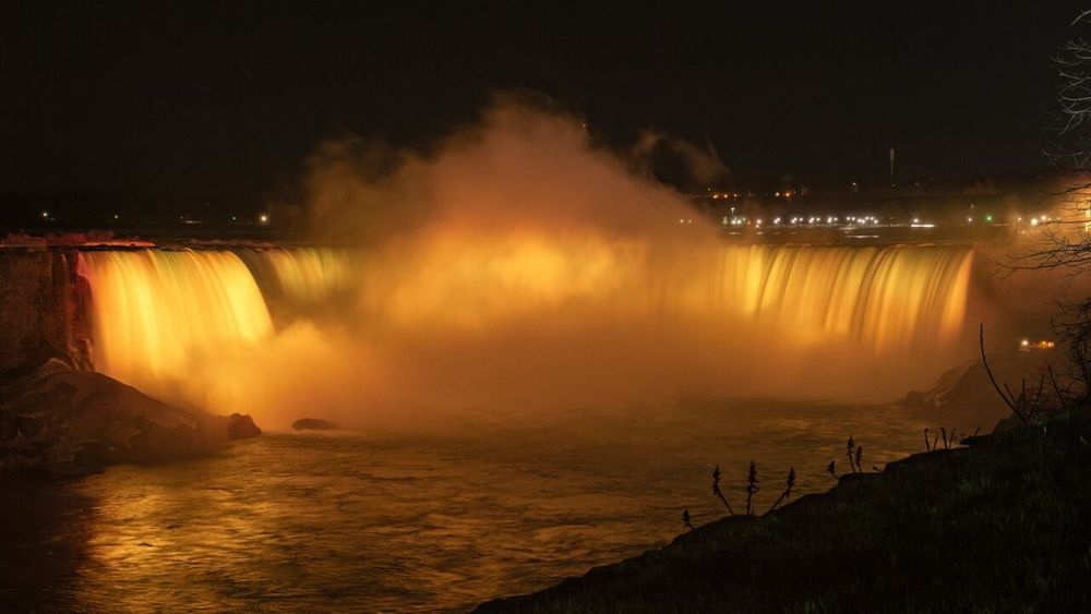 photograph of niagara falls at night, illuminated with yellow light