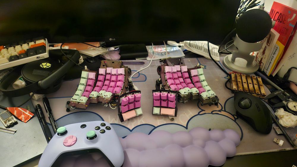 Messy desk covered in electronics, showing off a pink and purple split keyboard.