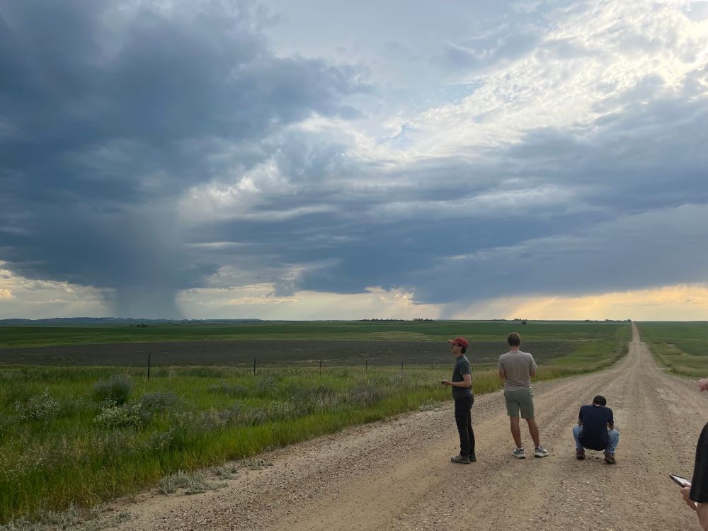 People on a dirt road watching distant showers