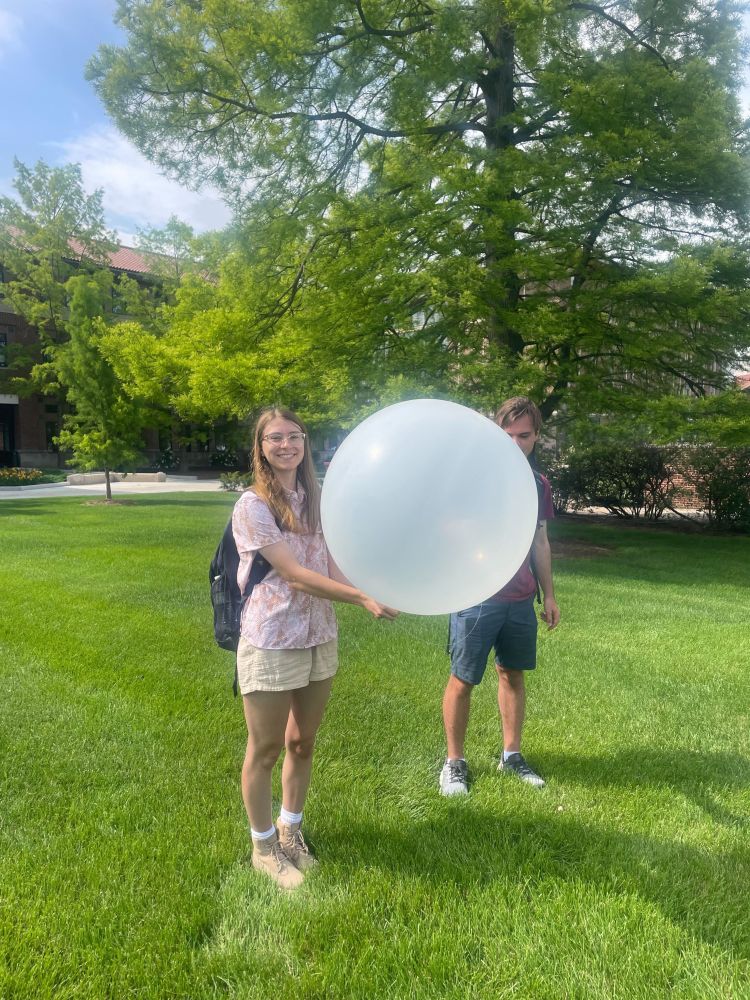 Two people standing on grass holding a large white balloon