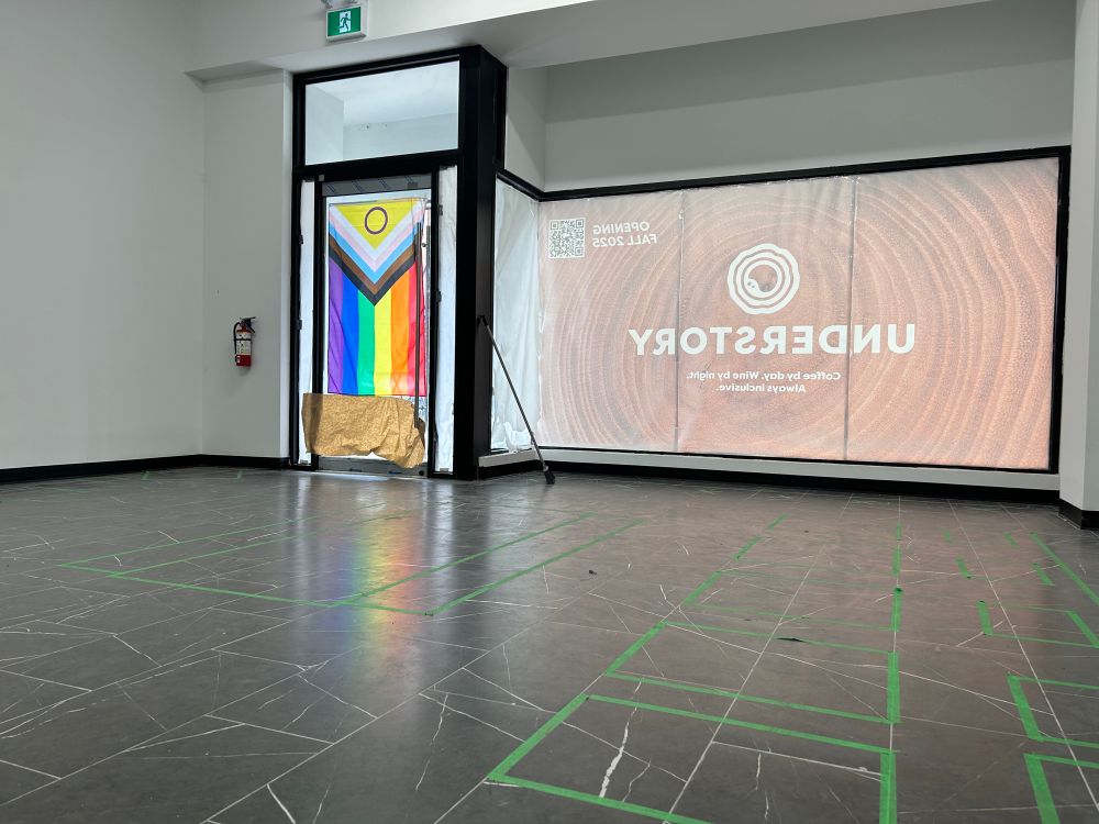 The inside of a retail space with white walls and a black tiled floor. A progress flag is hanging in the door. 
