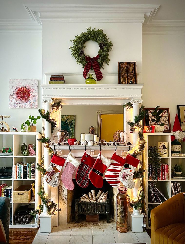 A living room fireplace with six stockings and wreath above it. Two bookshelves hug the sides.