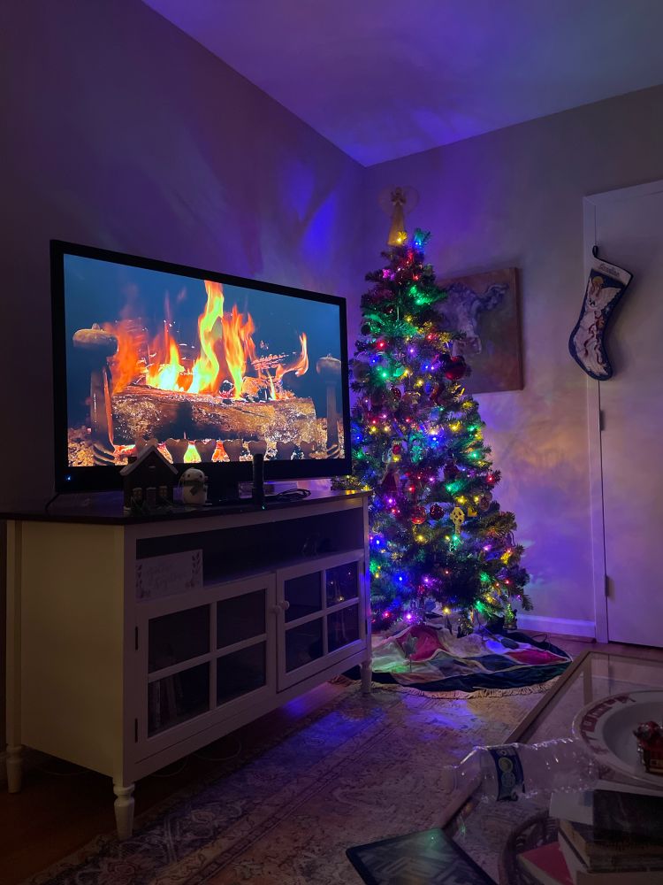 A picture of a fireplace on a TV with a colorful Christmas tree in the background. Very cozy. 