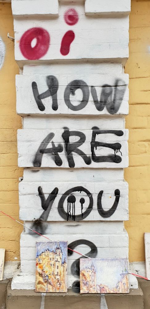 Graffiti written on the wall: Oi How Are You? in big all caps letter. Below the writing are two paintings of The Richard's Castle. Photo taken in the streets of Kyiv, Ukraine.