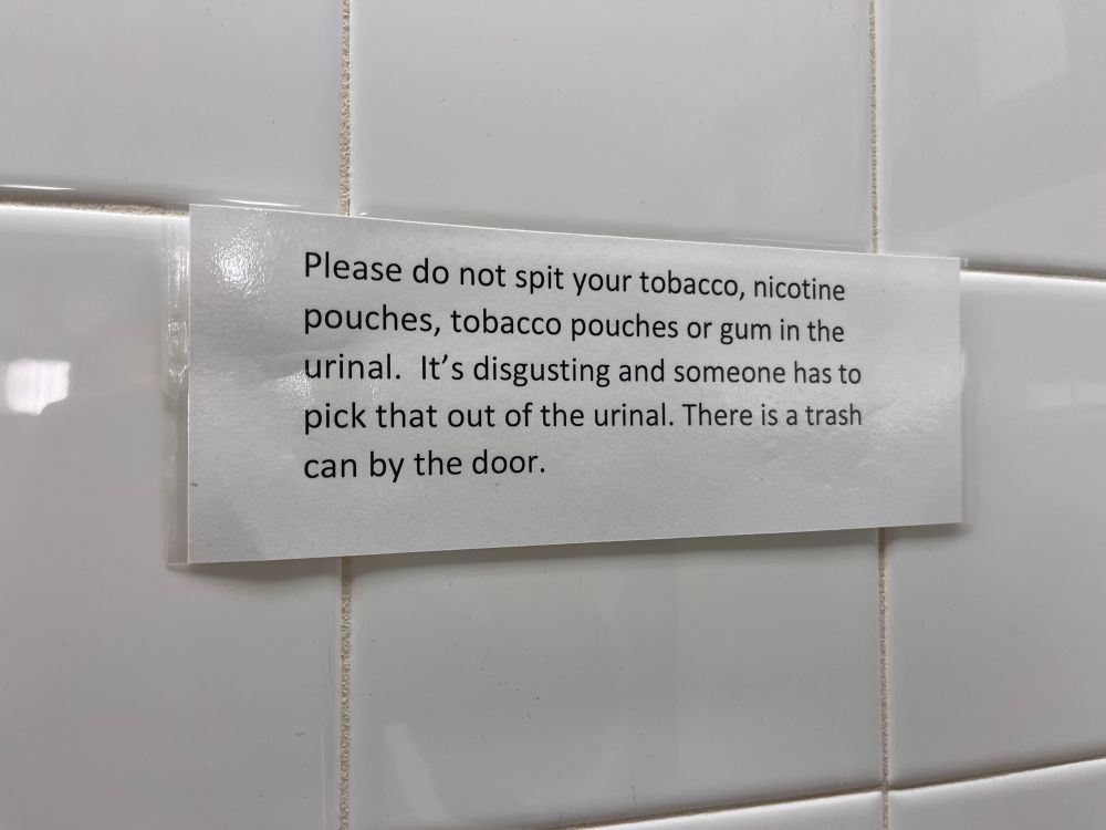 Printed sign hung on the bathroom wall: please do not spit your tobacco, nicotine pouches, tobacco pouches, or gum in the urinal. It’s disgusting and someone has to pick that out of the urinal. There is a trashcan by the door.