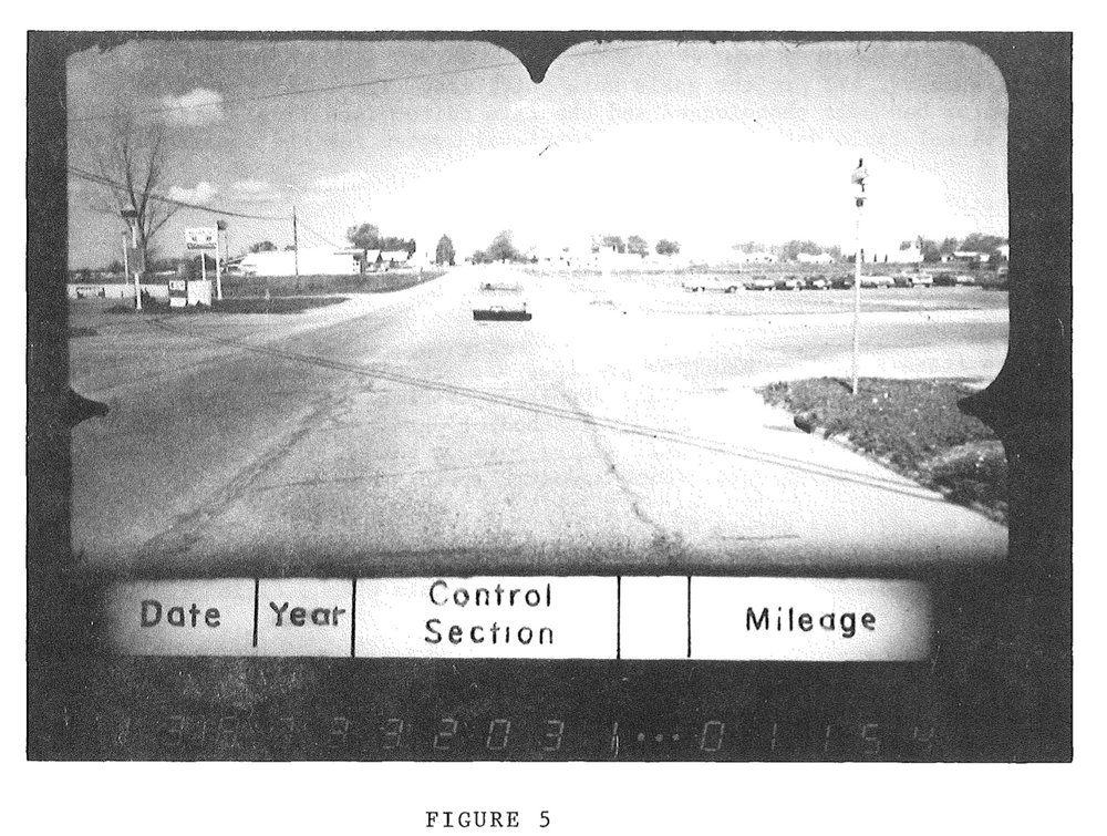 A black and white image of an intersection with a lone car in the distance and a visible control section banner at the bottom.