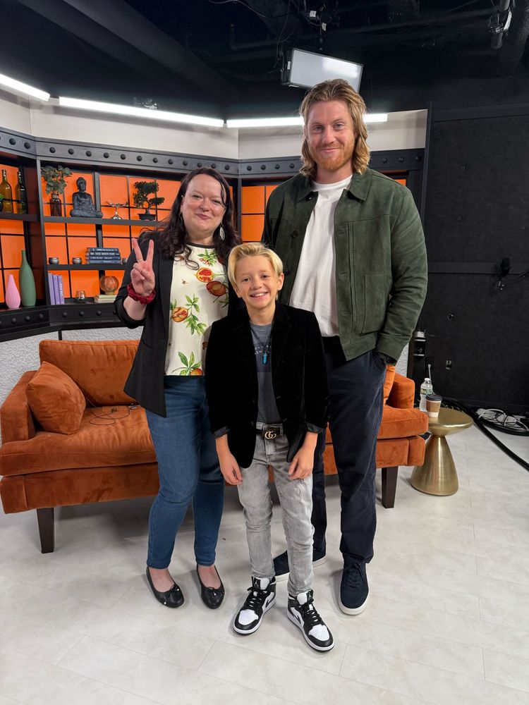 A doofus named Meghan giving the peace sign, standing next to A KNIGHT OF THE SEVEN KINGDOMS stars Dexter Sol-Ansell (Egg) and Peter Claffey (Dunk) in the Decider studio - orange couch and orange screen and white floor in background