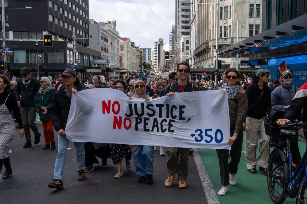 Photo of 350 volunteers walking in large protest crowd. Four people are holding a banner that reads “No Justice, No Peace” in black and red and a small 350 logo on the bottom right corner