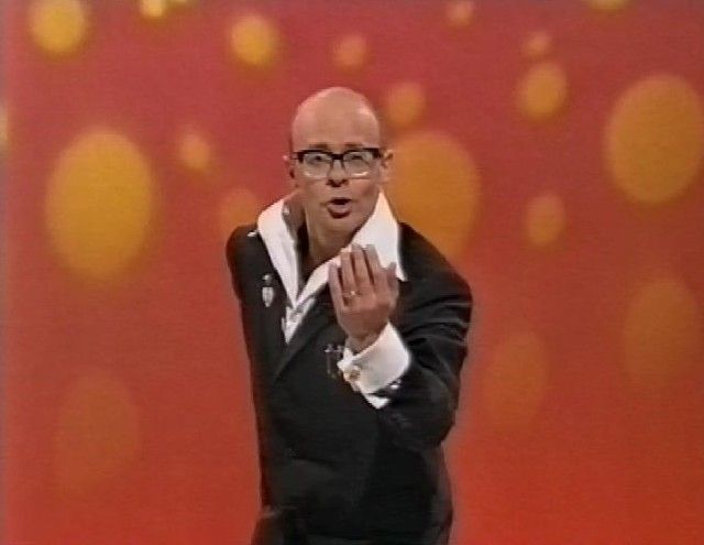 Harry Hill pointing his fingers up.