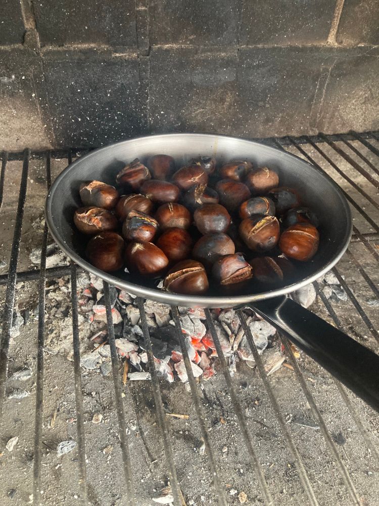 Castañas asándose en una sartén con orificios sobre brasas de carbón.