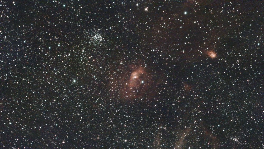 Image shows many stars, a star cluster and extensive dust/gas clouds the Bubble nebula is in the centre, tinged red.