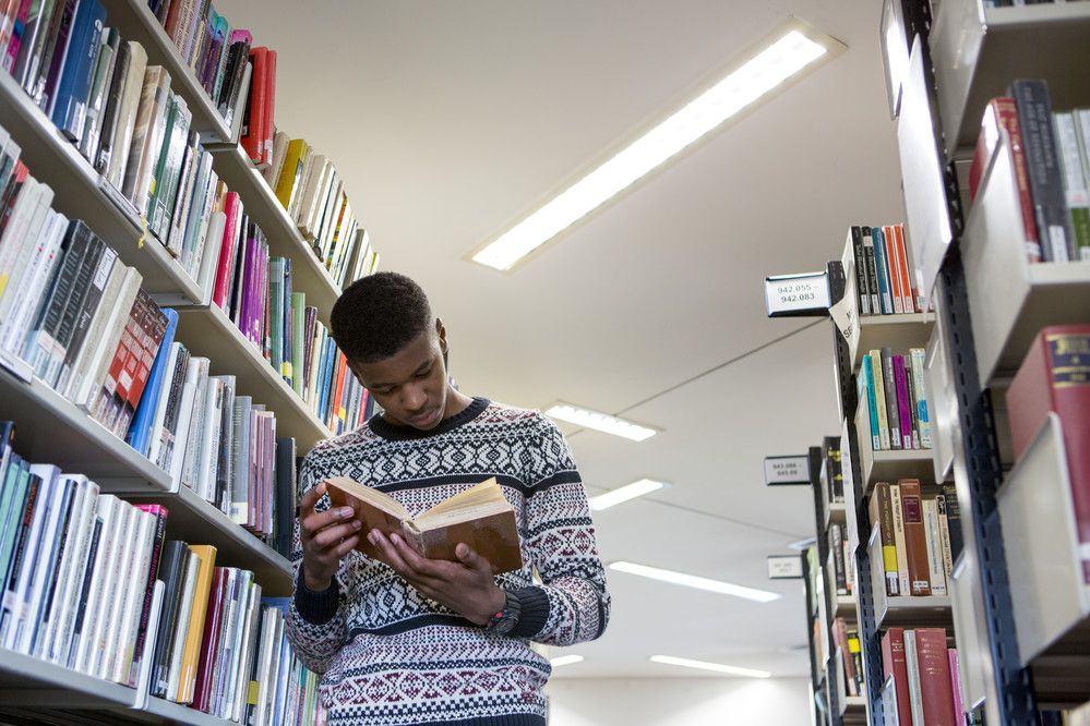 A student reading among shelves in Goldsmiths Library.