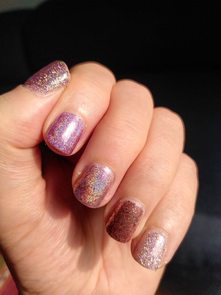 Left hand showing skittle manicure with all pale pink purple nailpolish all in different sparkly or metallic finish