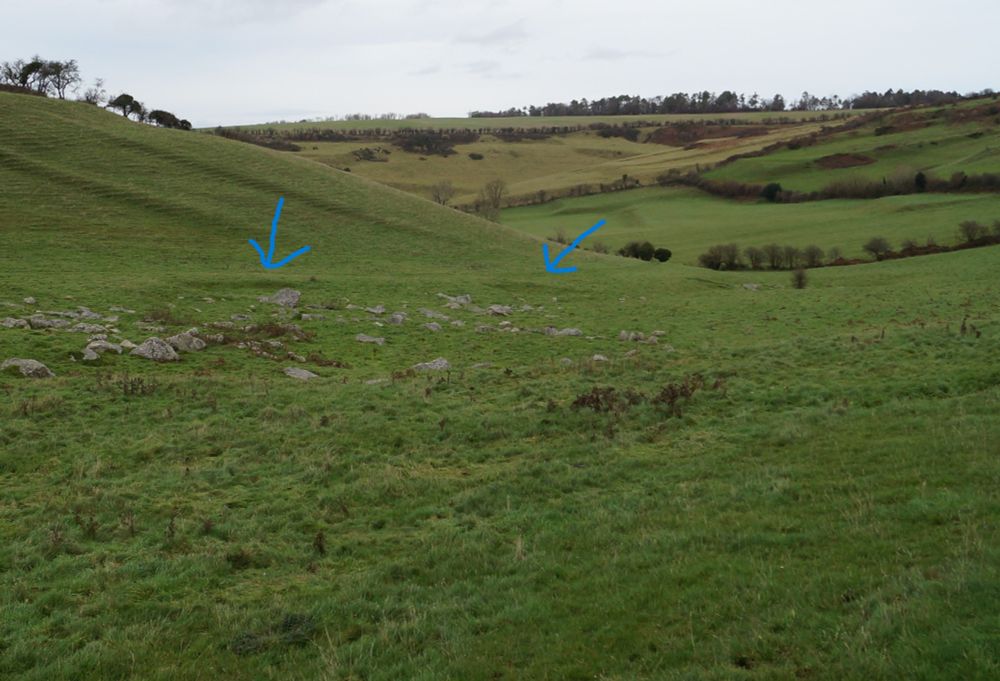 In a grass valley some banks are visible near a collection of large stones