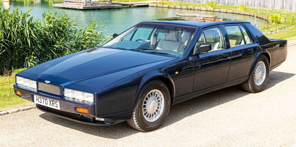 An Aston Martin Lagonda on a gravel roadway by a lake. 