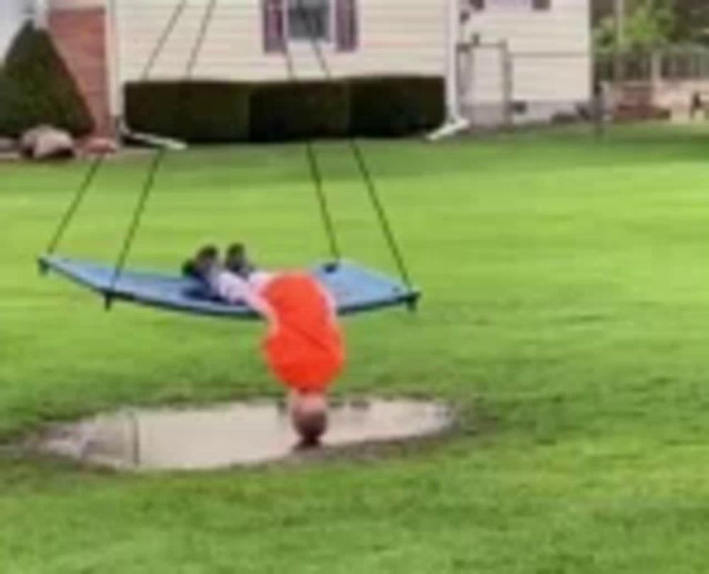 a child is doing a handstand on a blue hammock in a yard .